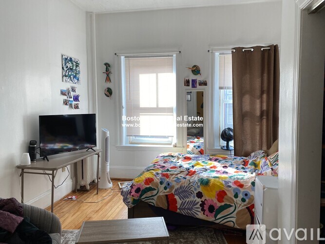 A bedroom with a bed, a television, and a window with blinds.