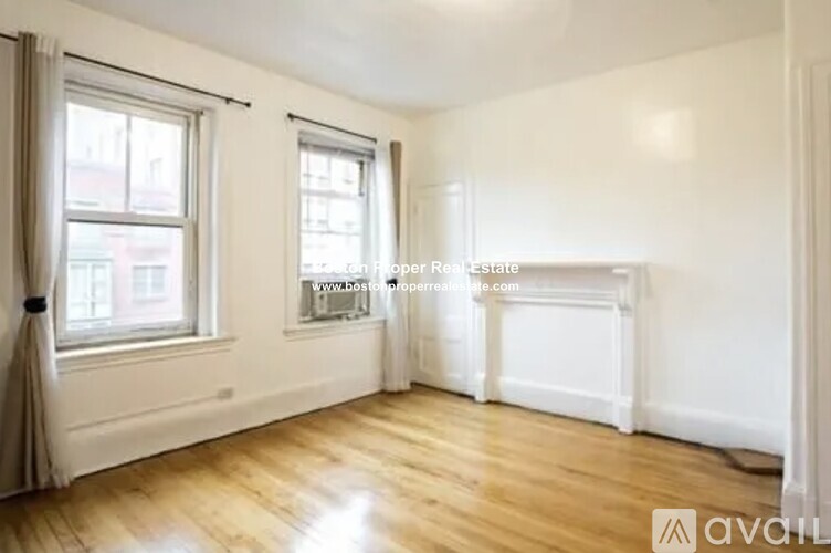 A room with wooden floors and white walls, with a window on the left and a door on the right.