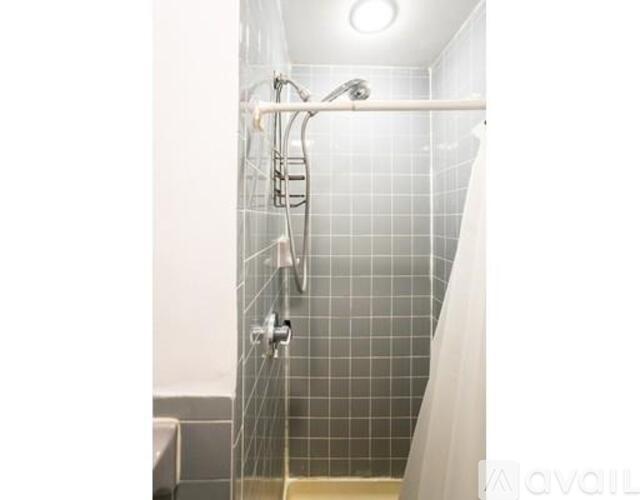 A shower with a white curtain and a grey tile wall.
