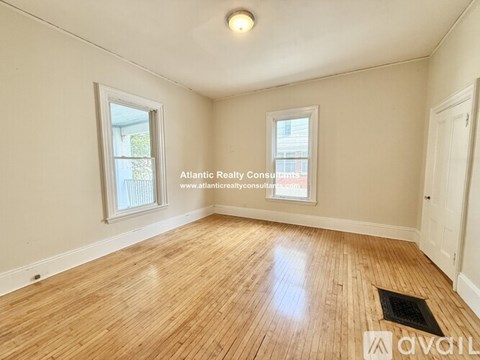 A room with wooden flooring and two windows.