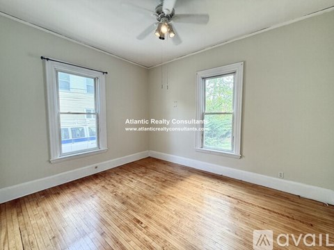 A room with wooden flooring and two windows, one of which has blinds.