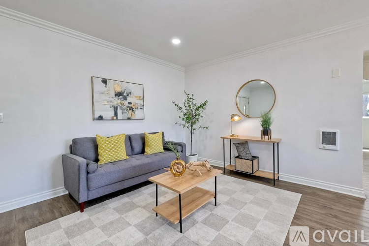 A living room with a grey couch, a coffee table, a small table with a mirror and a plant, and a rug on the floor.
