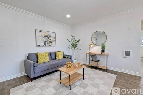 A living room with a grey couch, a coffee table, a small table with a mirror and a plant, and a rug on the floor.