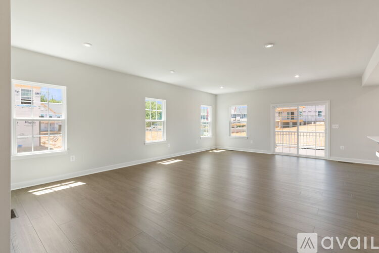A spacious room with wooden flooring and white walls, featuring a large window and a door leading to a balcony.