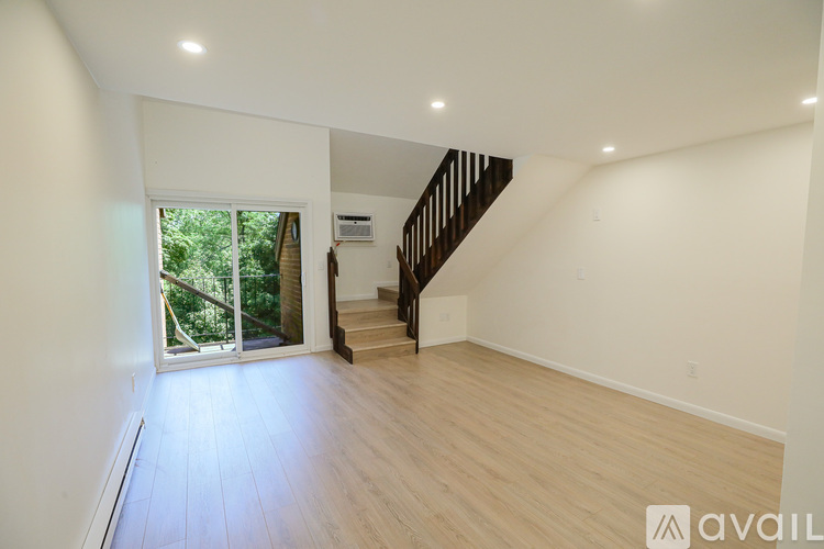 A spacious room with wooden flooring and a staircase leading to another level.