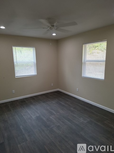 A room with a ceiling fan and two windows.