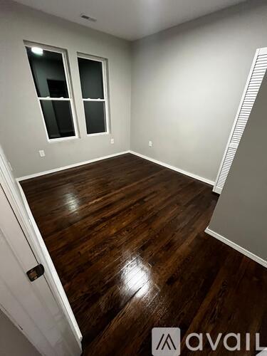 A room with wooden flooring and two windows.