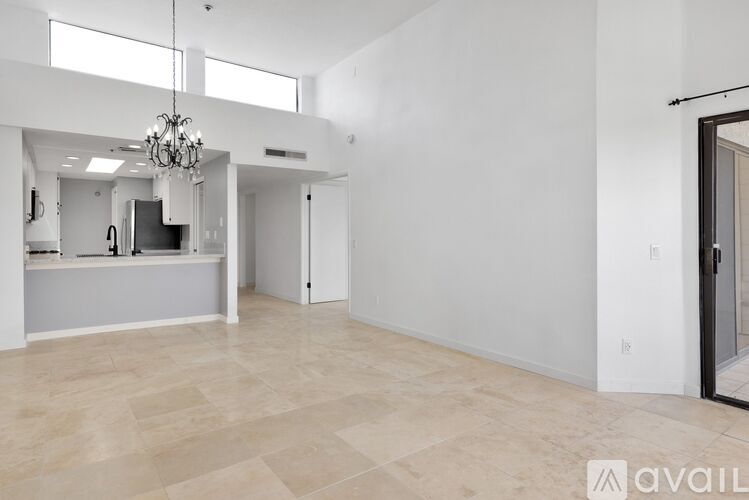 A spacious living room with a chandelier and a kitchen area in the background.