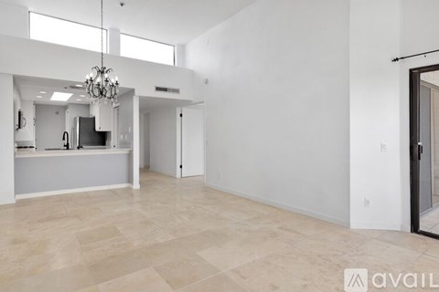 A spacious living room with a chandelier and a kitchen area in the background.