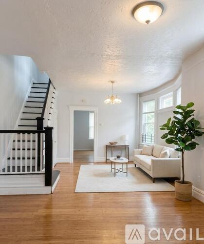 A living room with a white couch, a coffee table, a potted plant, and a staircase.