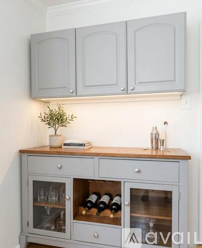 A grey cabinet with a wooden top and glass doors is filled with wine bottles.