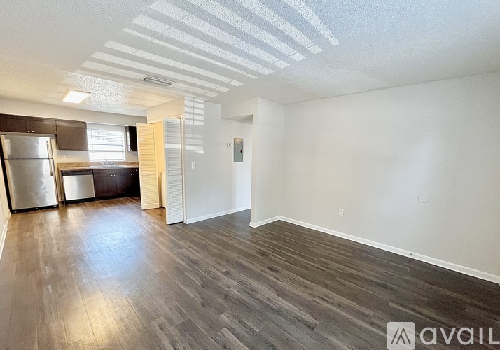 A room with wooden flooring and a kitchen area with a refrigerator, sink, and cabinets.