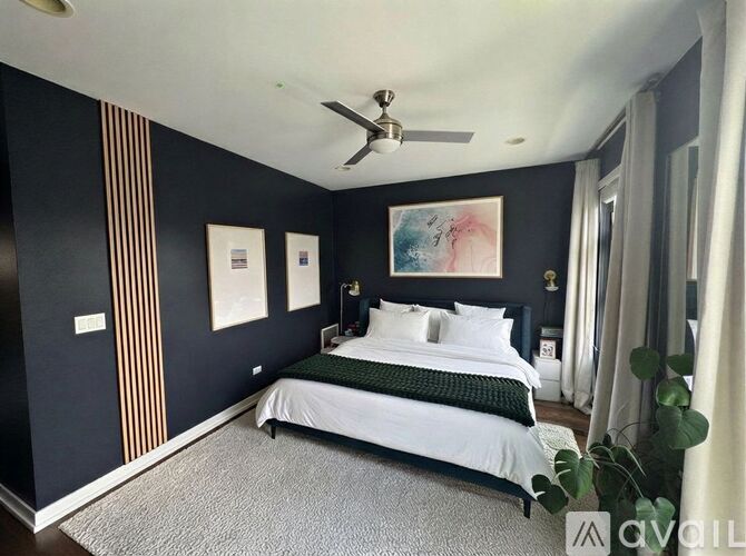 A bedroom with a bed, a ceiling fan, and a painting on the wall.