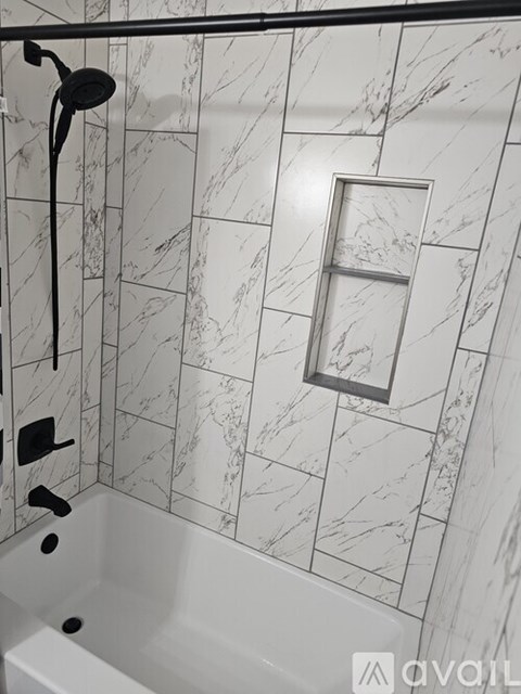 A white bathtub with a black shower head and a marble wall.