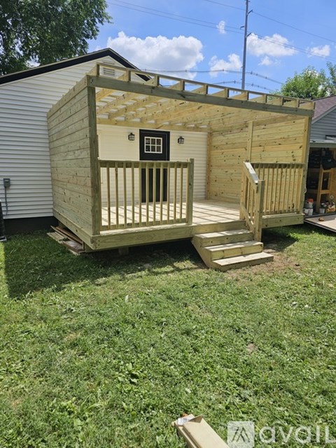 A wooden shed with a door and windows is being built in a backyard.