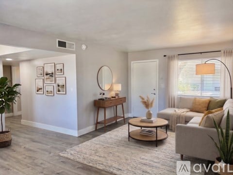 A living room with a grey couch, a wooden coffee table, and a round mirror on the wall.