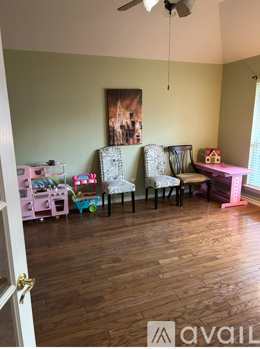 A room with a pink chair and a painting of a castle on the wall.