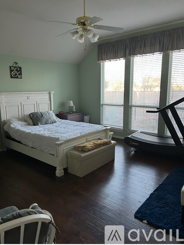 A bedroom with a bed, a bench, a fan, and a window with blinds.