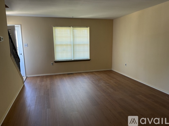Empty room with wooden flooring and a window with blinds.