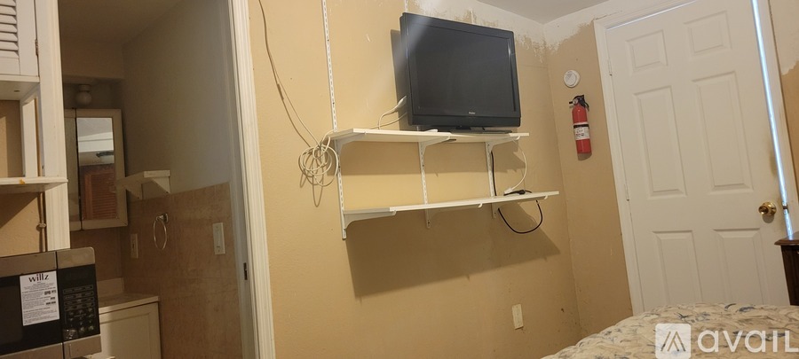 A small room with a bed, a microwave, a TV, and a fire extinguisher.