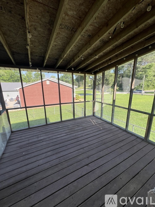 A wooden deck with a glass railing and a view of a red building and green lawn.