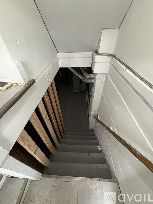 A staircase with a wooden handrail and concrete steps leading to a dark space.