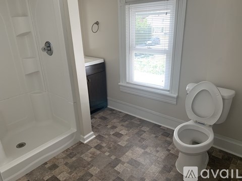 A white toilet is in a bathroom with a tiled floor and a window.