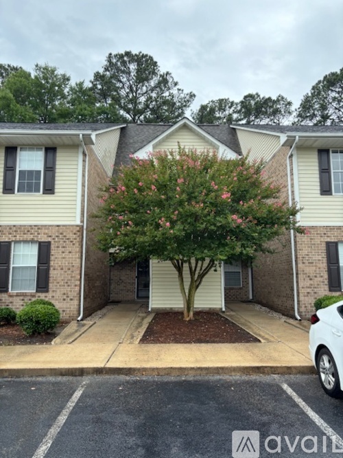 A tree with pink flowers is in front of a two-story apartment building.
