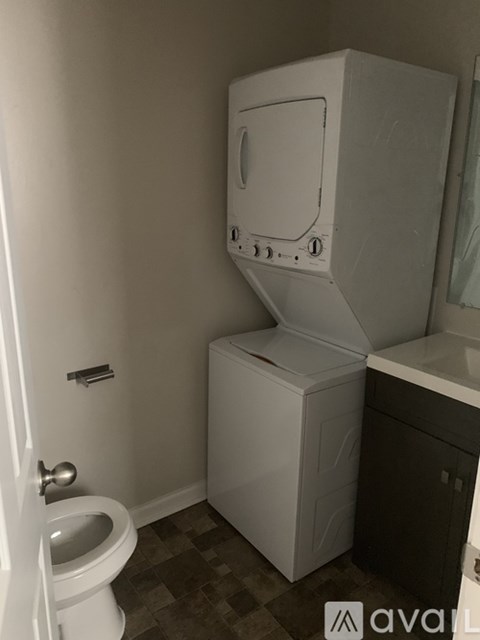 A white toilet sits next to a white washer and dryer in a small bathroom.