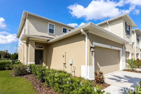 A beige house with a white garage door and a small garden in front.