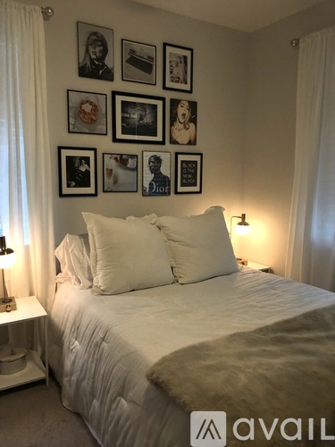 A bedroom with a bed, two pillows, a nightstand with a lamp, and a wall with framed pictures.