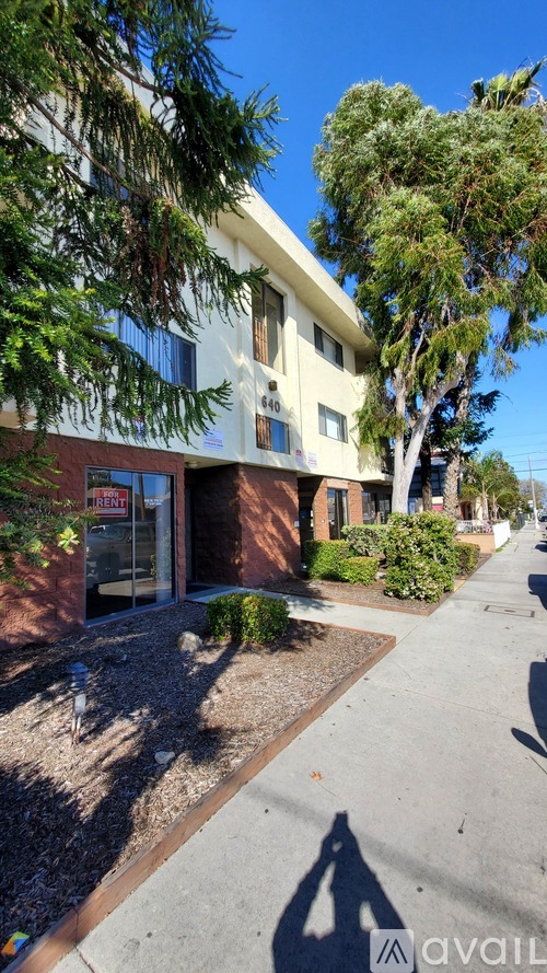 A building with a red sign that says "For Sale" is surrounded by trees and bushes.