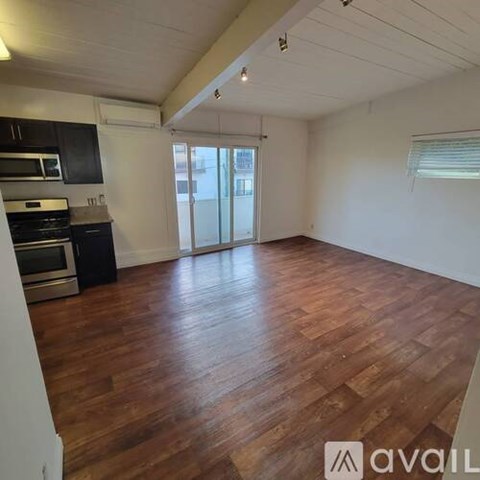 A spacious room with wooden flooring and a kitchen area with stainless steel appliances.