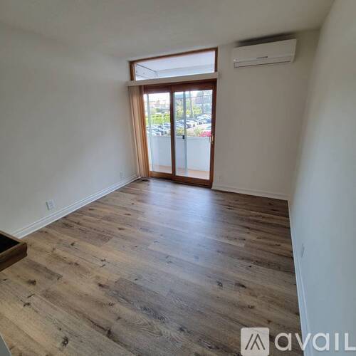 A room with wooden flooring and a sliding glass door leading to a parking lot.