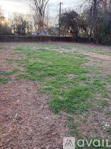 A grassy field with a fence and trees in the background.