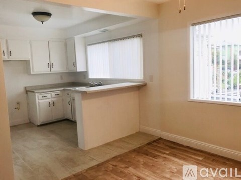 A kitchen with white cabinets and a window with blinds.