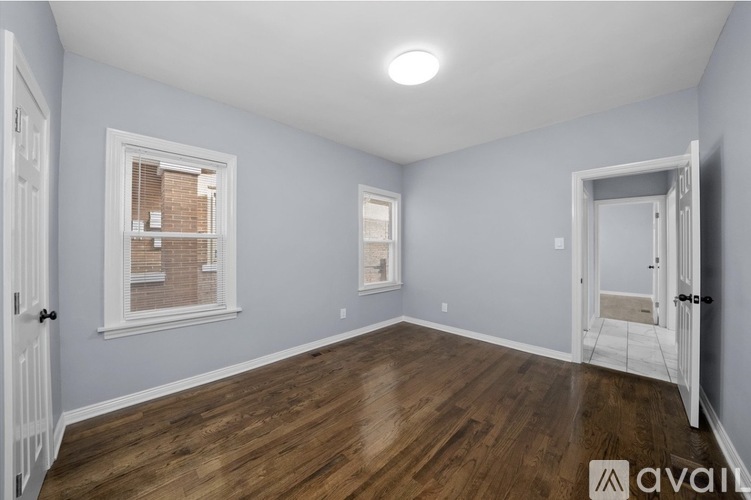 A room with wooden floors and white walls, with a window showing a brick building outside.