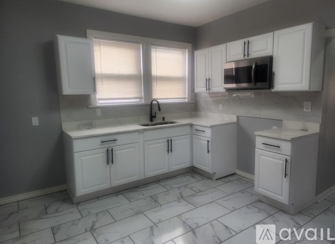 A kitchen with white cabinets and marble flooring.