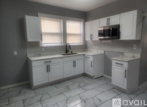 A kitchen with white cabinets and marble flooring.