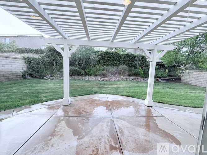 A patio with a white pergola and concrete floor.