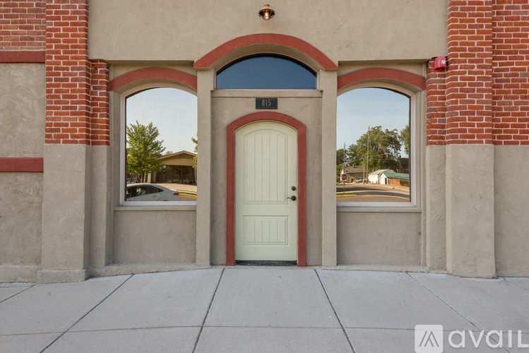 A white door is flanked by two windows in a brick building.