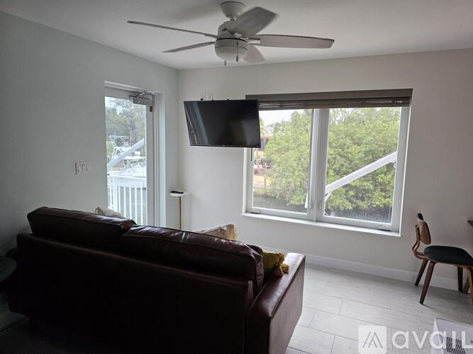 A living room with a brown couch, a fan, and a flat screen TV mounted on the wall.