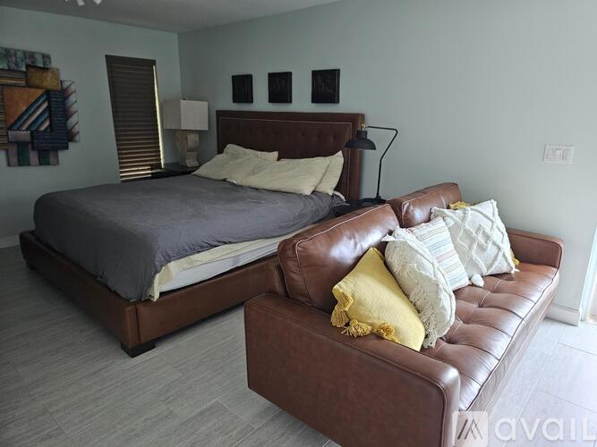 A bedroom with a brown leather couch and a bed with a grey bedspread.