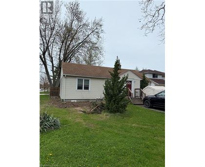 A house with a white siding and a brown roof is surrounded by a green lawn and a tree.