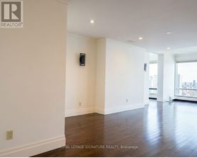 A spacious room with wooden floors and white walls, featuring a large window with a city view.