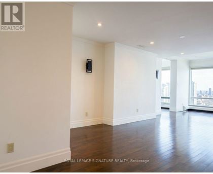 A spacious room with wooden floors and white walls, featuring a large window with a city view.