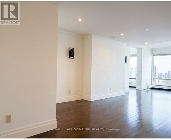 A spacious room with wooden floors and white walls, featuring a large window with a city view.