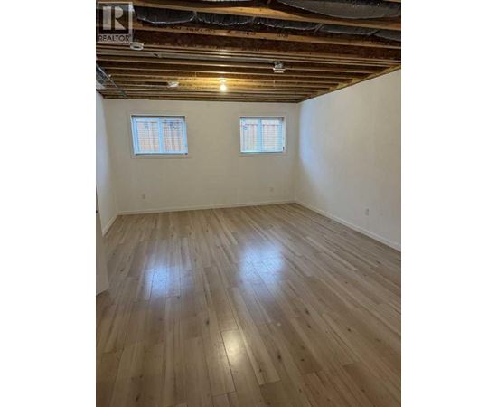 A room with wooden flooring and two windows.