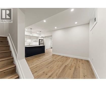 A spacious room with wooden flooring and a staircase on the left side.