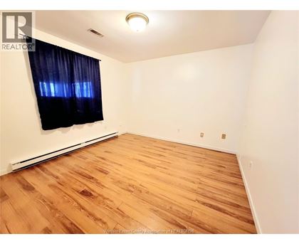 A room with wooden flooring and a window with black curtains.